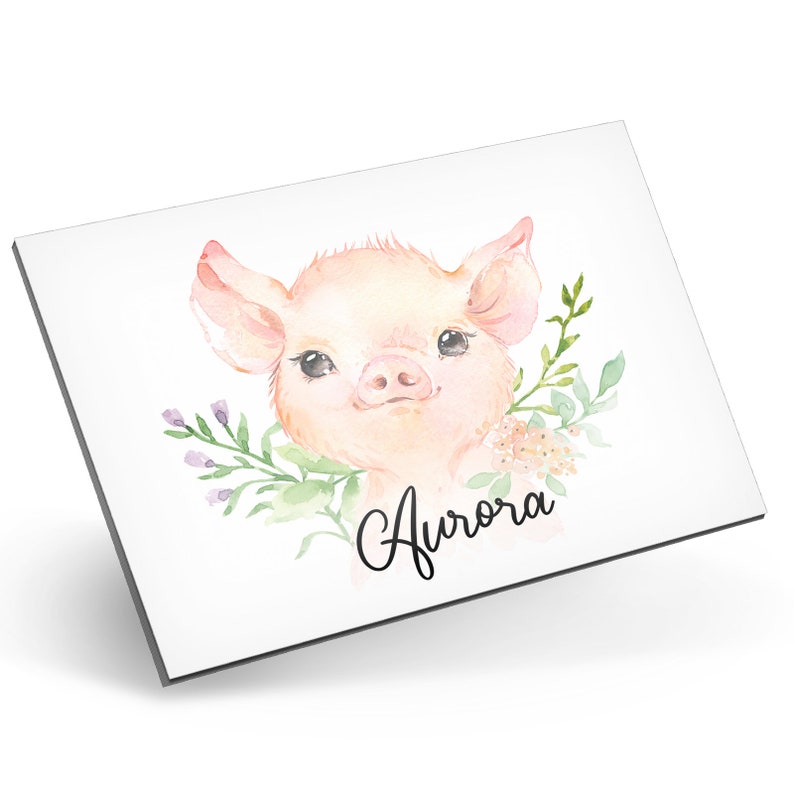 Puede incluir: Una ilustraci&oacute;n de acuarela de un lech&oacute;n rosado con una corona de flores alrededor de su cabeza. El lech&oacute;n est&aacute; mirando al espectador con una expresi&oacute;n dulce. El nombre "Aurora" est&aacute; escrito en cursiva debajo del lech&oacute;n.