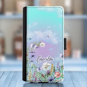 Può includere: Una custodia per telefono blu e viola con un design floreale e il nome "Camilla" stampato su di essa.