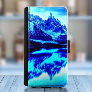 May include: A blue and white phone case with a mountain range reflected in a lake. The mountains are a dark blue and the lake is a light blue.