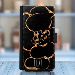 May include: Black phone case with a gold glitter floral design and the name "LEXI" printed in white.