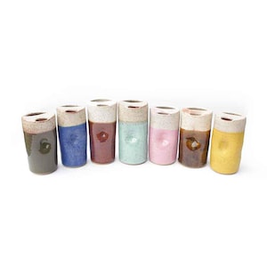 May include: A collection of seven ceramic tumblers in various colors. Each tumbler has a cylindrical shape with a white top and a colored lower half. Colors include green, blue, burgundy, mint, pink, brown, and yellow.