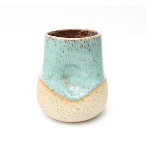 May include: A speckled light blue and beige ceramic mug with a rounded bottom.