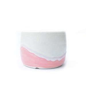 May include: A white ceramic mug with a pink painted base and a soft transition to the white upper section. The mug has a simple, rounded shape and a smooth, glossy finish. Suitable for coffee, tea, or other drinks.