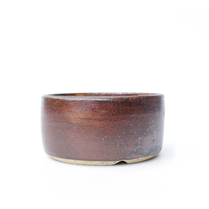 May include: A handcrafted, round ceramic bowl with a rich, earthy brown glaze. The bowl has a low profile and a speckled texture, with a lighter beige base. This pottery piece is ideal for serving or as a decorative accent.