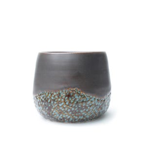 May include: A dark brown ceramic tumbler with a textured, turquoise and brown speckled base. The upper portion of the cup is a smooth, solid dark brown. The cup has a rounded shape and is set against a white background.