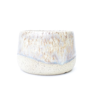 May include: A ceramic planter with a speckled, off-white base and a glazed top. The top section features a blend of white, tan, and light blue hues, creating a textured, layered appearance. The planter has a rounded shape.