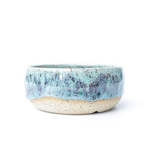 May include: A set of three ceramic nesting bowls in shades of blue, green, and white. The bowls feature a speckled glaze and a simple, modern design. The largest bowl is approximately 7 inches in diameter.