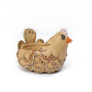May include: A ceramic chicken planter with a speckled brown glaze and a white glaze on the feathers. The chicken has a pink comb and wattle, orange beak, and green eyes.