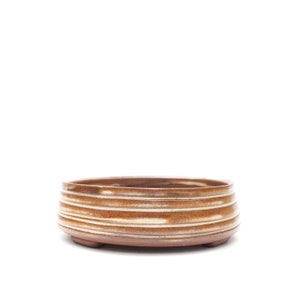 May include: A handcrafted, low, round ceramic bowl with a brown and tan striped design. The bowl has a slightly textured surface and sits on three small feet. The interior is a darker brown, and the exterior features horizontal stripes.