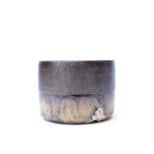 May include: A handmade ceramic cup, featuring a textured dark brown upper section and a lighter, mottled lower half. The cylindrical cup has a rustic, artisanal appearance. The glaze has a subtle sheen, enhancing the design's depth and character.