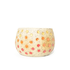 May include: A rounded ceramic planter with a speckled beige base featuring a gradient pattern of small, raised dots in shades of yellow, orange, and pink. The vessel has a wide, open top and a smooth, curved exterior surface.
