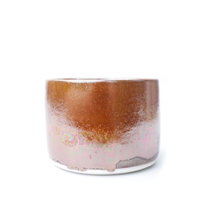 May include: A small, cylindrical ceramic pot with a glossy, iridescent finish. The pot transitions from a warm brown at the top to a shimmering, multi-colored base. The interior is white, and the pot sits on a white base.