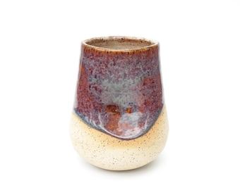 May include: A ceramic cup with a speckled, light brown glaze on the bottom and a dark brown and purple glaze on the top.