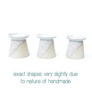 May include: Three handmade ceramic candle holders. Each has a speckled white top and a diagonal color block design in white and beige. The text at the bottom reads "exact shapes vary slightly due to nature of handmade."
