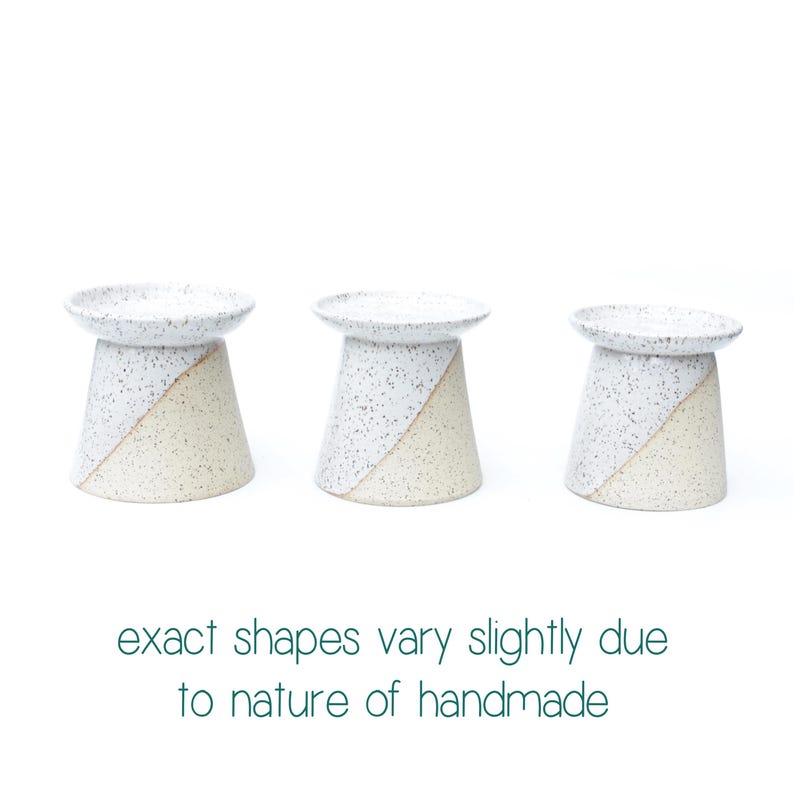 May include: Three handmade ceramic candle holders. Each has a speckled white top and a diagonal color block design in white and beige. The text at the bottom reads "exact shapes vary slightly due to nature of handmade."