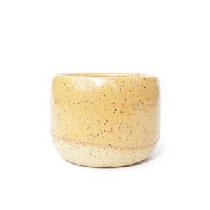 Puede incluir: Una taza cilíndrica de cerámica con un esmalte amarillo moteado en la parte superior y un acabado moteado de color crema más claro en la base inferior. El recipiente tiene un borde liso y redondeado y una base sólida y estable.