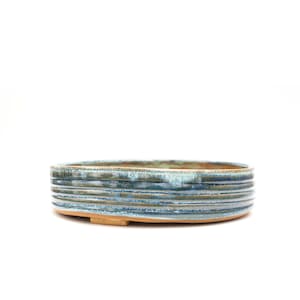 May include: A blue and brown glazed ceramic bonsai pot with a rounded oval shape and a slightly raised rim. The pot has a textured surface with horizontal lines.
