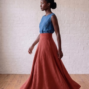 May include: A sleeveless blue top paired with a high-waisted, floor-length rust-colored skirt. The skirt features a wide waistband and a full, flowing silhouette that reaches the floor, crafted from a textured fabric with visible weave details.