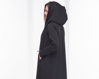 May include: A long black hooded cardigan with vertical ribbed detailing. The cardigan has a long, flowing silhouette and a large hood.