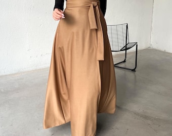 Op de afbeelding: Een bruine wikkelrok met een lange, vloeiende silhouet. De rok heeft een brede tailleband met een strik die aan de voorkant in een strik kan worden geknoopt. De rok wordt gecombineerd met een zwart longsleeve turtleneck shirt.