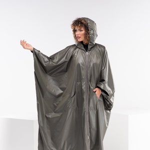 May include: A long, olive green hooded raincoat with a zipper closure and a large pocket on the front. The raincoat is made of a shiny, water-resistant material.