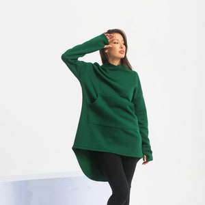 May include: A woman wearing a dark green hooded sweatshirt with a long, asymmetrical hemline and black leggings. She is wearing black lace-up boots.