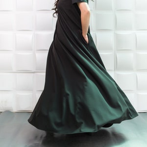 K&ouml;nnte beinhalten: Eine Frau tr&auml;gt ein langes, flie&szlig;endes schwarzes Kleid mit kurzen &Auml;rmeln. Das Kleid hat ein schlichtes Design und ist aus einem weichen, flie&szlig;enden Stoff gefertigt. Die Frau steht vor einer wei&szlig;en gekachelten Wand.