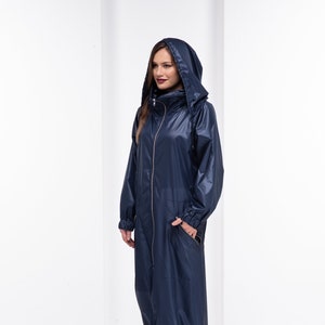 May include: A long navy blue raincoat with a hood and a zipper closure. The raincoat has a drawstring at the waist and elastic cuffs. The model is wearing black boots.