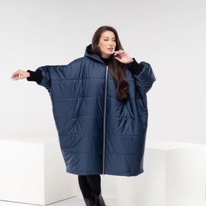 Könnte beinhalten: Eine marineblaue Kapuzen-Steppjacke mit Reißverschluss. Die Jacke hat eine lockere Passform und ist durchgehend gesteppt. Das Model trägt eine schwarze Leggings und schwarze Stiefel.
