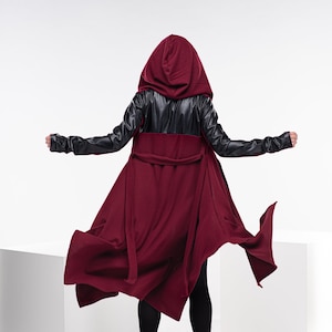 May include: A long, burgundy hooded coat with black leather sleeves. The coat has a tie belt and a flowing, asymmetrical hem.