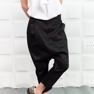 Puede incluir: Una persona que lleva pantalones negros con un ajuste holgado y recogido y zapatos de cordones metálicos dorados.