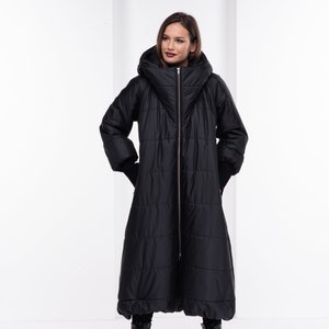 May include: A long black puffer coat with a large hood and a zipper closure. The coat has a quilted design and is worn with black boots.