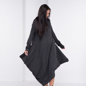 May include: A long, charcoal gray, asymmetrical dress with long sleeves and a cowl neck. The dress is made of a soft, stretchy fabric and has a relaxed fit. The model is wearing black ankle boots.