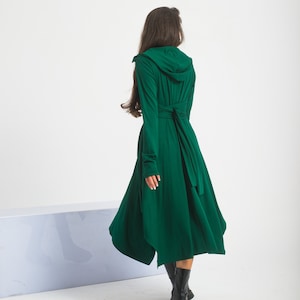 Könnte beinhalten: Ein langes, dunkelgrünes Kapuzenkleid mit einem Bindegürtel. Das Kleid hat einen fließenden, asymmetrischen Saum.