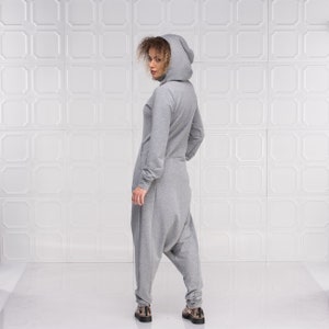 May include: A gray hooded jumpsuit with a relaxed fit and a drawstring hood. The jumpsuit has long sleeves and a relaxed fit in the legs.