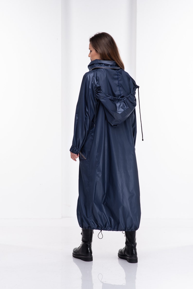 May include: A long, navy blue raincoat with a drawstring hood. The raincoat has a zipper closure and a cinched waist.