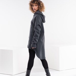 May include: A charcoal gray hooded sweatshirt with a long, asymmetrical hemline. The sweatshirt has a relaxed fit and a kangaroo pocket.