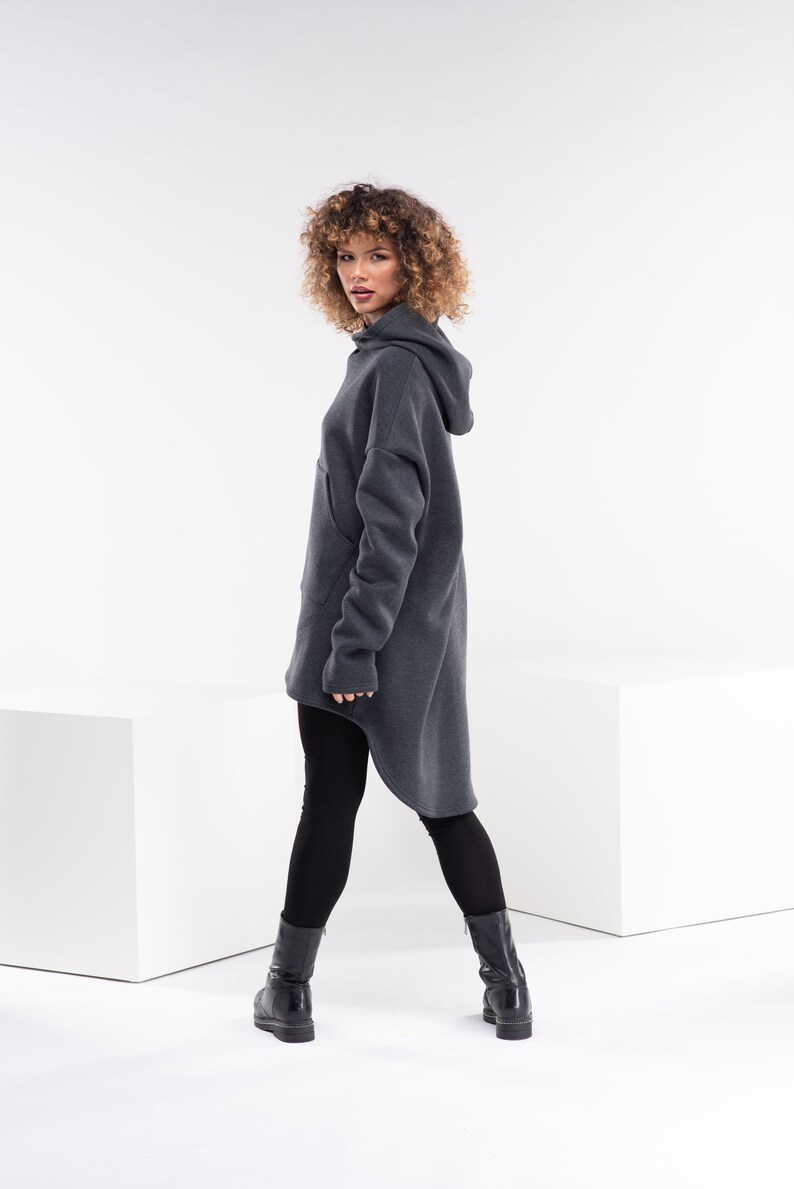 May include: A charcoal gray hooded sweatshirt with a long, asymmetrical hemline. The sweatshirt has a relaxed fit and a kangaroo pocket.