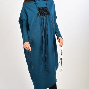 May include: A teal blue long-sleeved dress with a black beaded necklace. The necklace has long strands of black cord hanging from it.