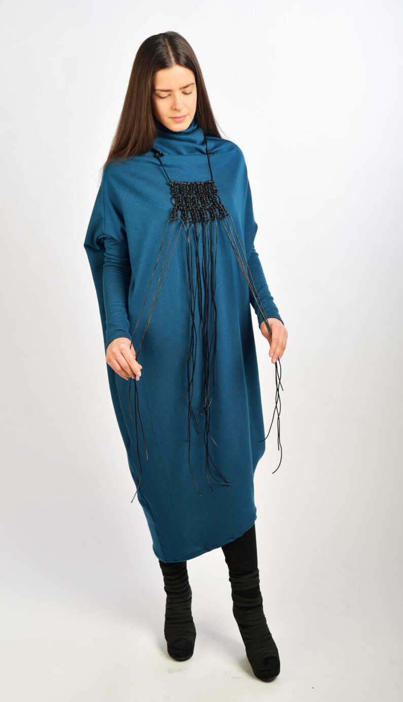 May include: A teal blue long-sleeved dress with a black beaded necklace. The necklace has long strands of black cord hanging from it.