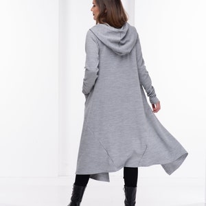 Pu&ograve; includere: Un lungo cardigan con cappuccio grigio con un orlo asimmetrico e fluido. Il cardigan &egrave; realizzato in un tessuto morbido e confortevole e ha una vestibilit&agrave; rilassata.