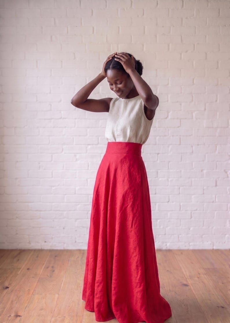 May include: A sleeveless cream-colored top paired with a high-waisted, floor-length red skirt. The top features a round neckline and a simple, fitted silhouette, while the skirt has a wide waistband and a full, flowing cut that reaches the floor.