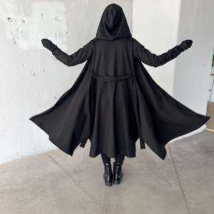 May include: A black hooded cloak with long sleeves and a waist tie. The cloak is open in the front, revealing black pants and boots. The person is standing with arms outstretched.