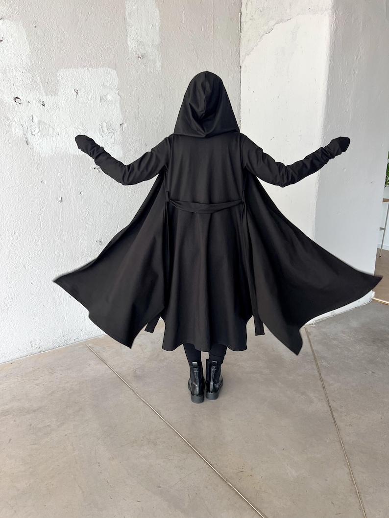 May include: A black hooded cloak with long sleeves and a waist tie. The cloak is open in the front, revealing black pants and boots. The person is standing with arms outstretched.