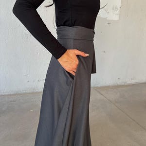 May include: A long, dark gray skirt with a wide waistband. The skirt is made of a soft, flowing fabric and has a slightly flared silhouette.