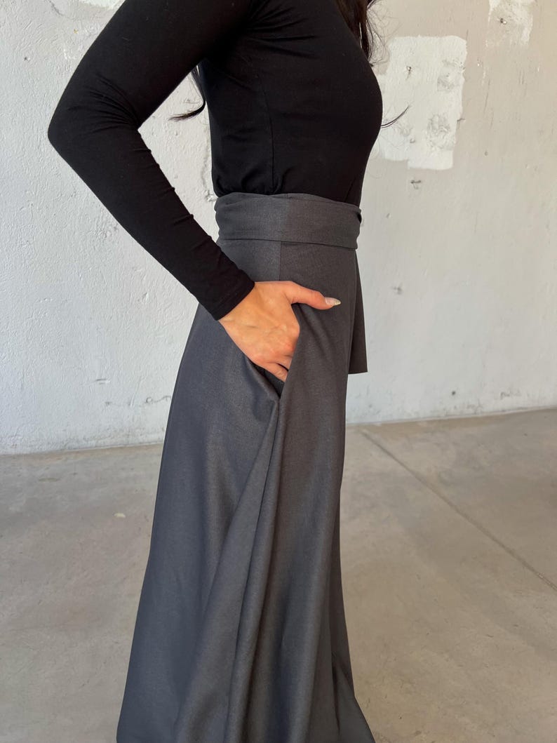May include: A long, dark gray skirt with a wide waistband. The skirt is made of a soft, flowing fabric and has a slightly flared silhouette.