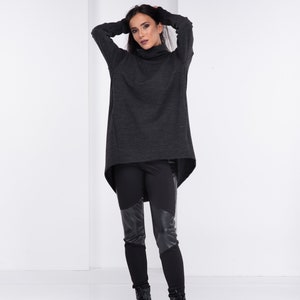 May include: A woman wearing a dark gray turtleneck sweater with a high-low hemline and black leggings with leather panels. She is wearing black ankle boots.