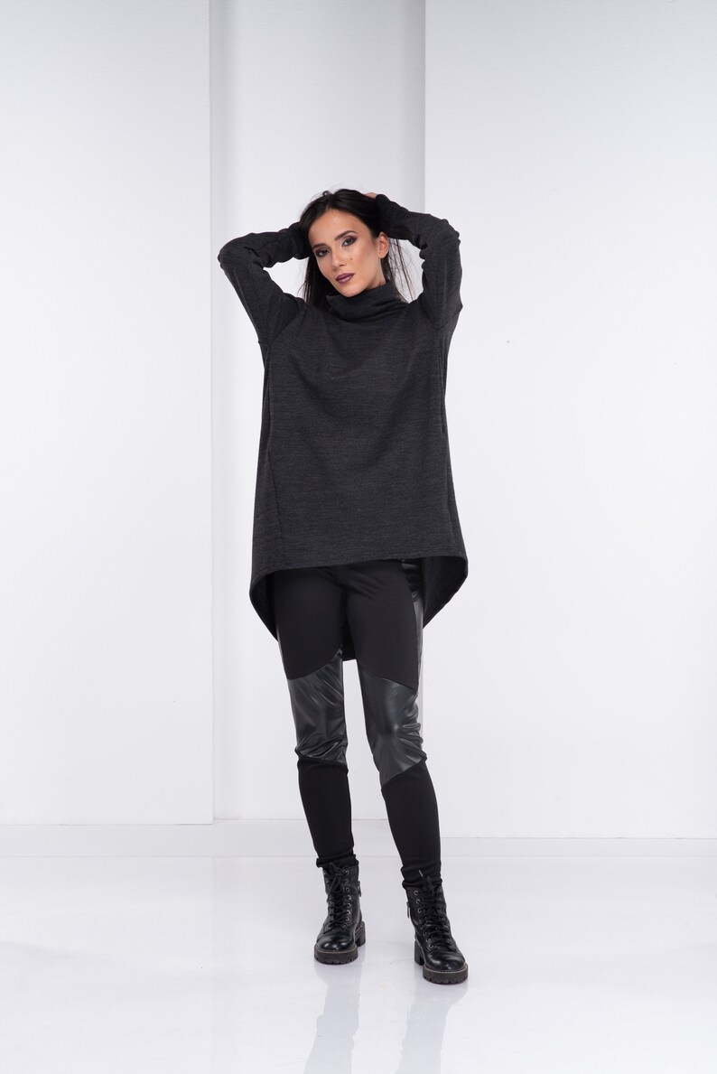 May include: A woman wearing a dark gray turtleneck sweater with a high-low hemline and black leggings with leather panels. She is wearing black ankle boots.