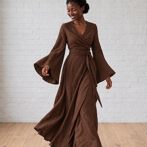 May include: A floor-length dark brown wrap dress featuring a V-neckline, long flared bell sleeves, and a matching fabric tie at the waist. The garment is crafted from a textured fabric and flows into a full, wide skirt that reaches the floor.