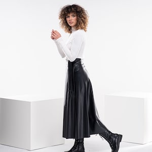 May include: A woman wearing a white turtleneck sweater and a black leather skirt. She is wearing black boots and has curly brown hair.